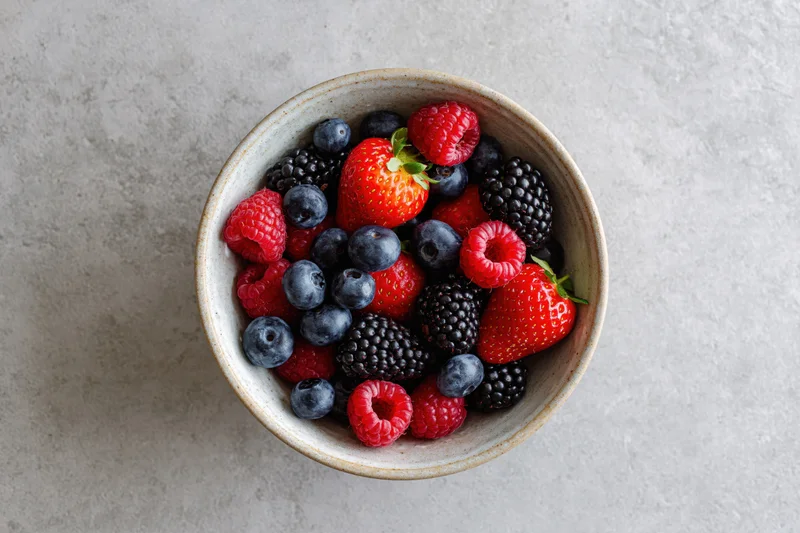 Ceramic bowl filled with mixed fresh berries on a gray countertop, top view