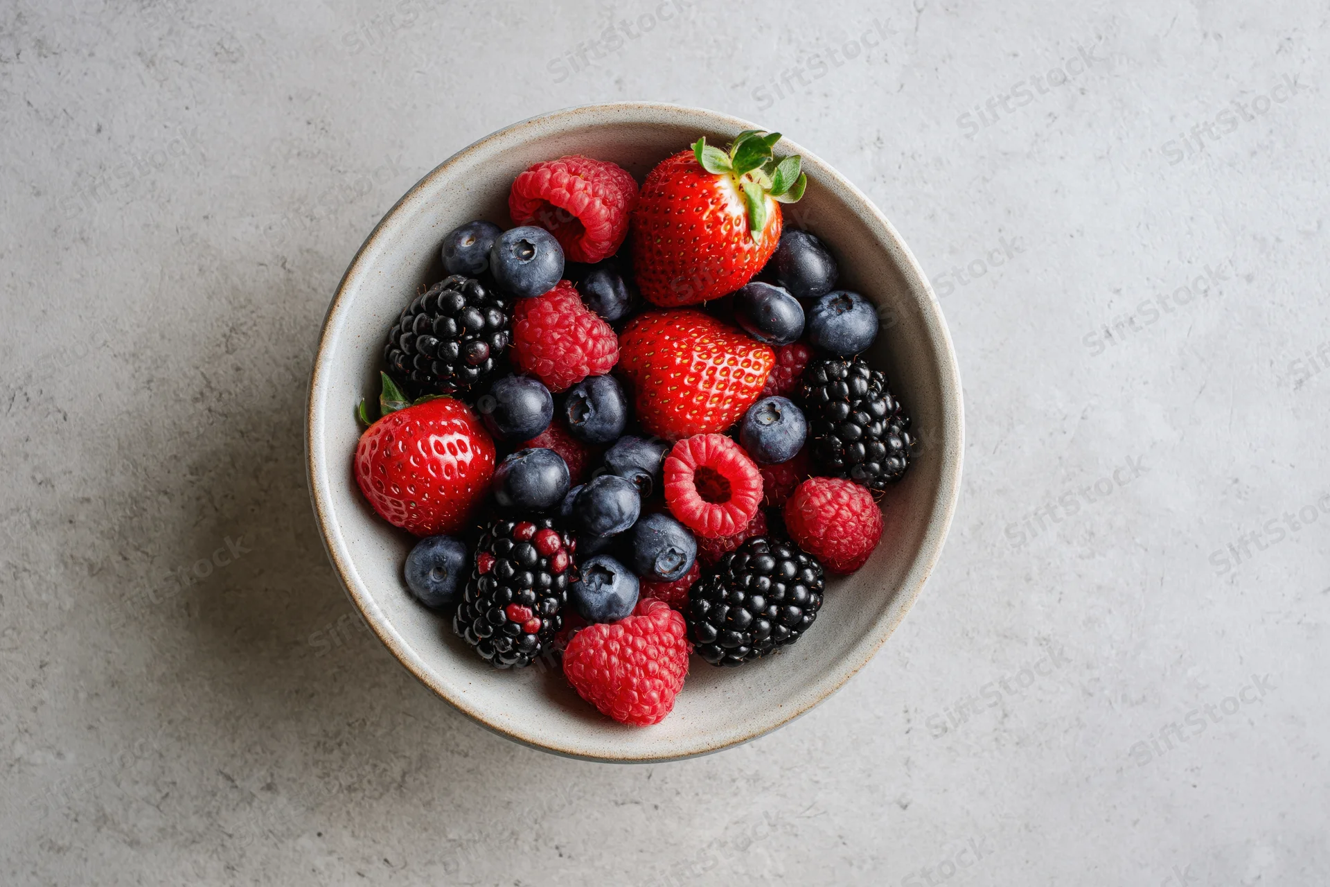 Ceramic bowl filled with mixed berries on a light gray surface