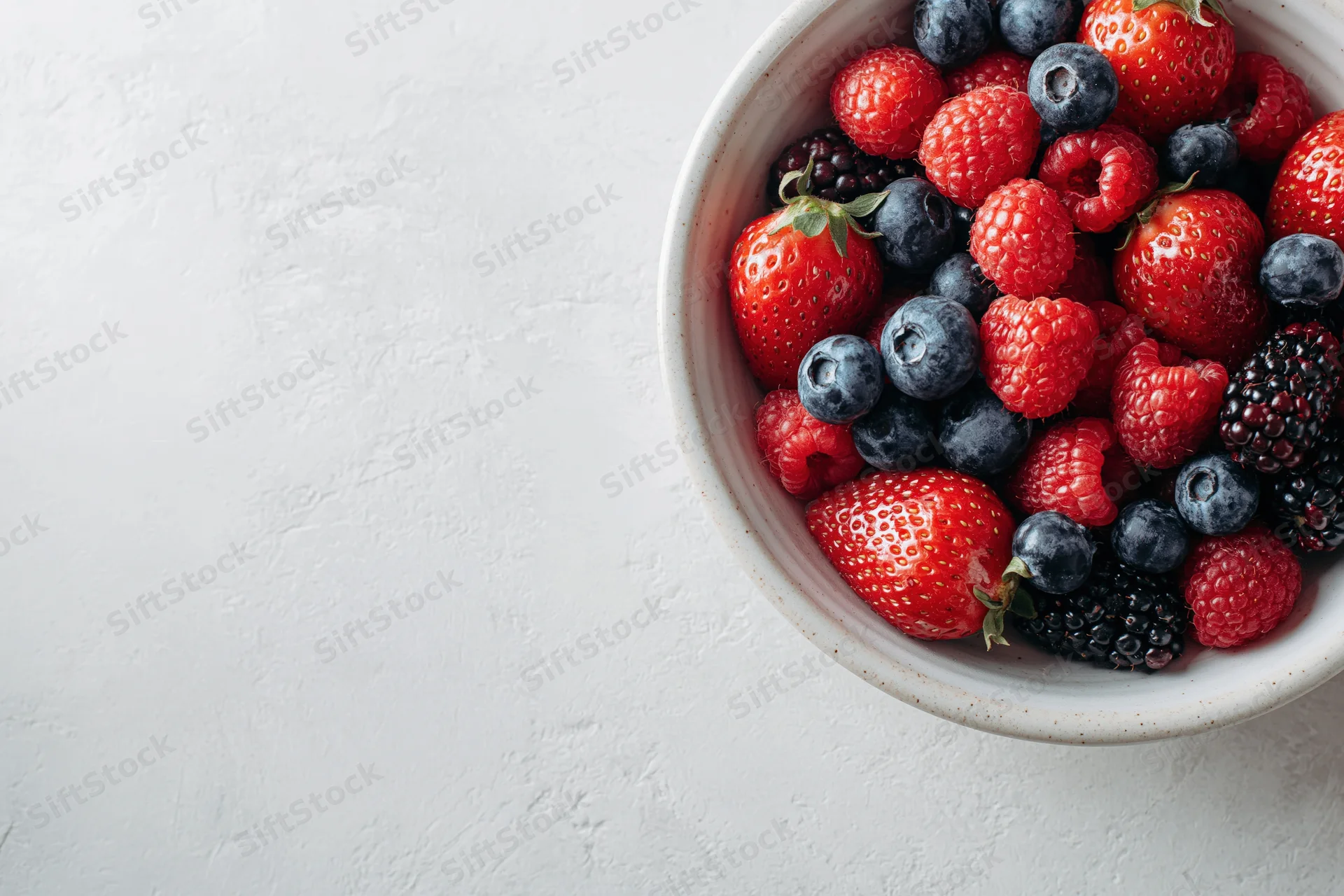 Ceramic bowl filled with mixed fresh berries on white textured surface