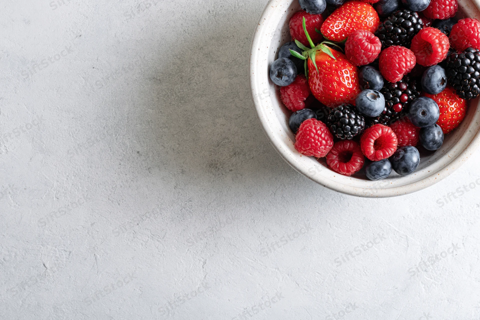 Ceramic bowl filled with mixed fresh berries on textured white surface