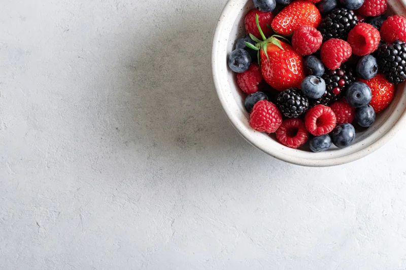 Ceramic bowl filled with mixed fresh berries on textured white surface