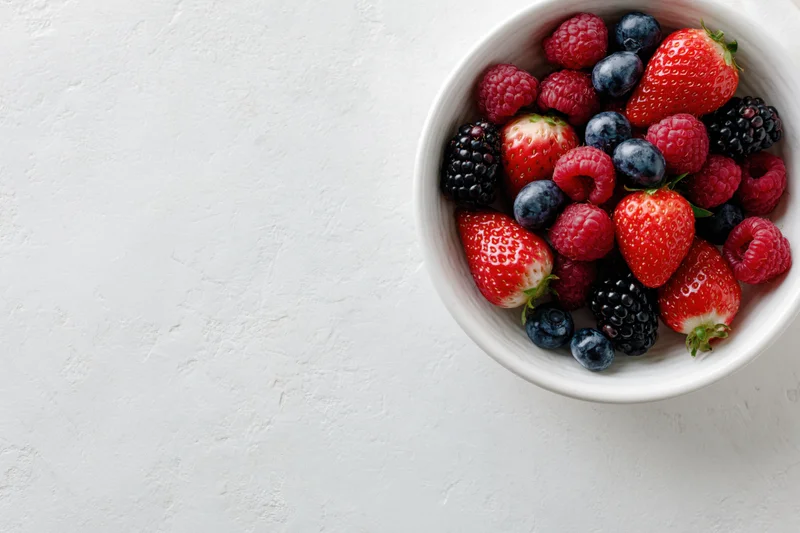 Mixed fresh berries in a white ceramic bowl on a textured white surface