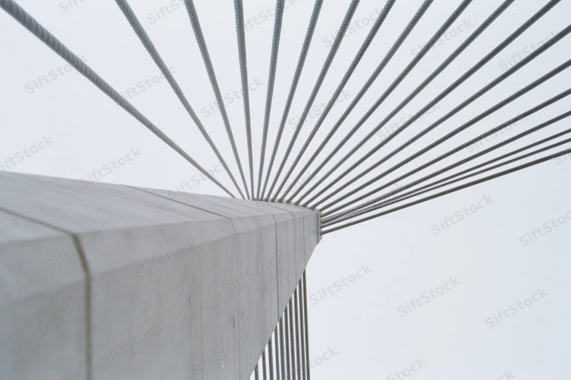 Low-angle view of cable-stayed bridge structure with concrete pillar and radiating steel cables against overcast sky