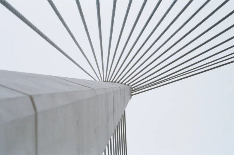 Low-angle view of cable-stayed bridge structure with concrete pillar and radiating steel cables against overcast sky