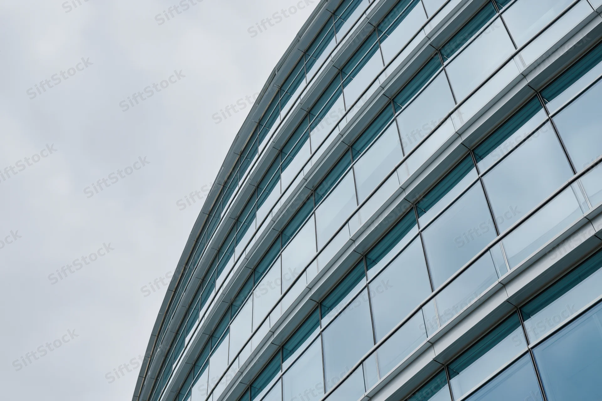 Curved glass curtain wall of modern office building against overcast sky
