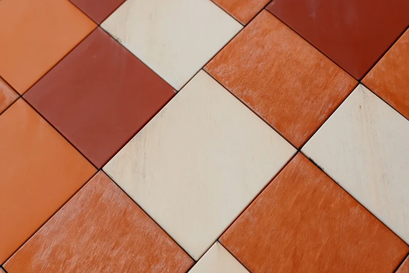 Close-up of orange and beige ceramic tiles arranged in a diagonal grid pattern on a modern building facade