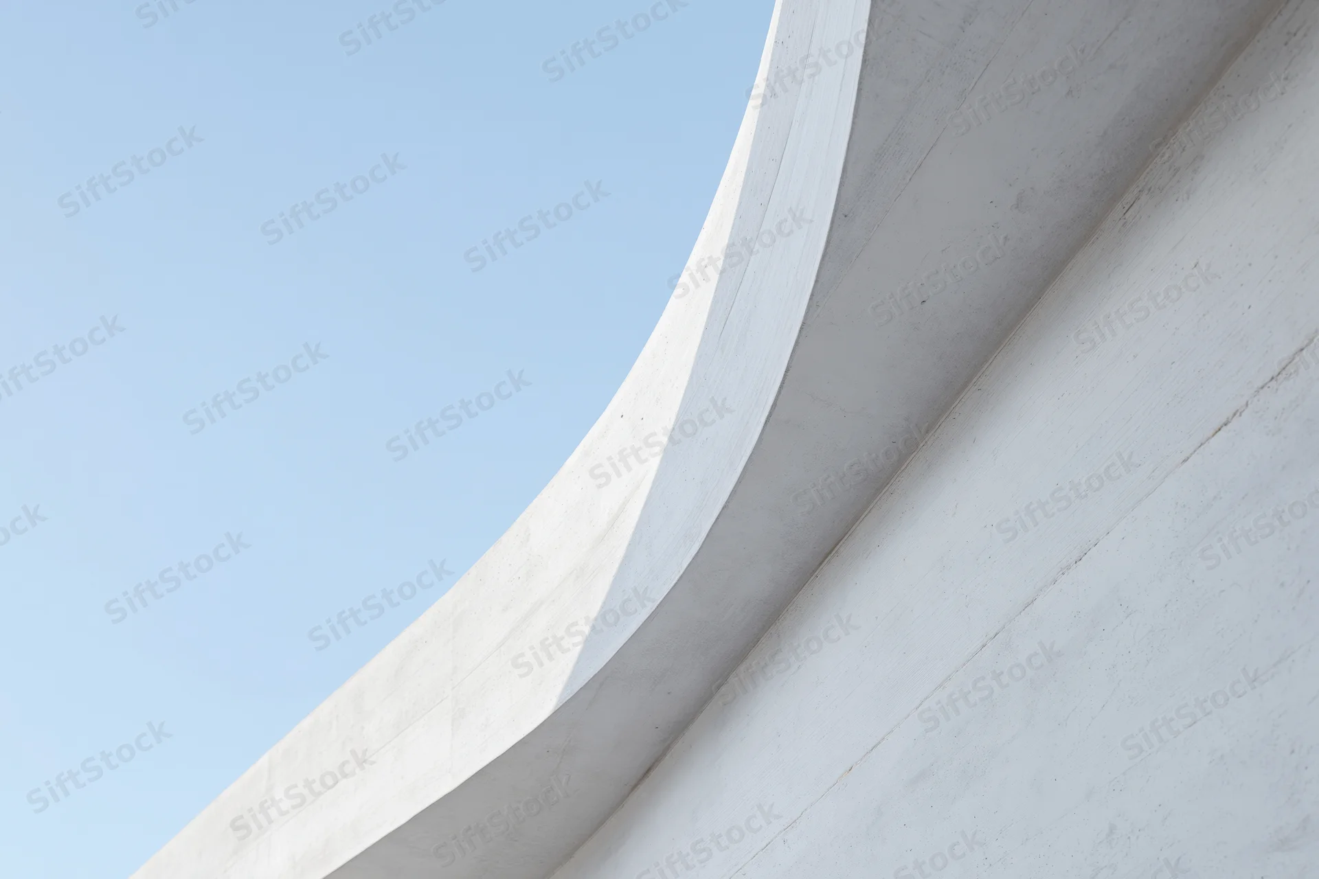 Curved white concrete facade of a modern building against a clear blue sky