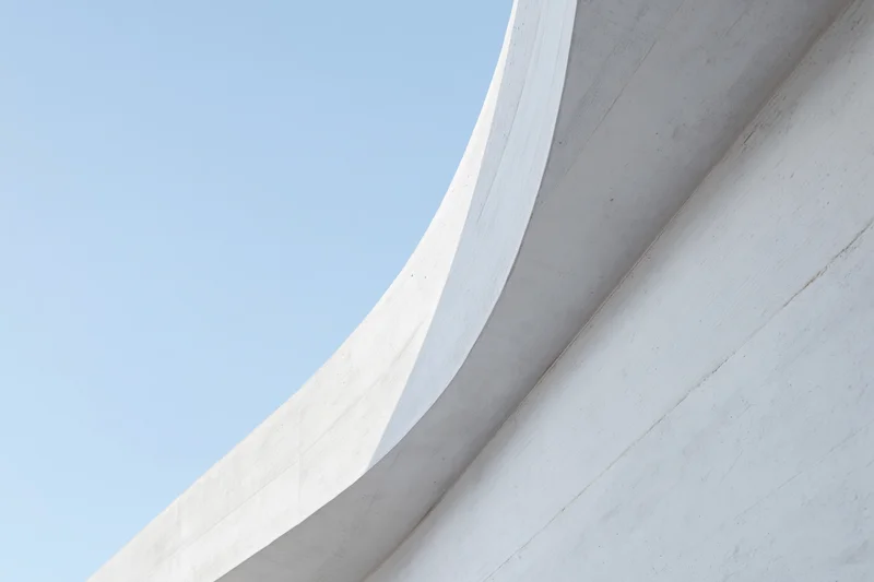 Curved white concrete facade of a modern building against a clear blue sky