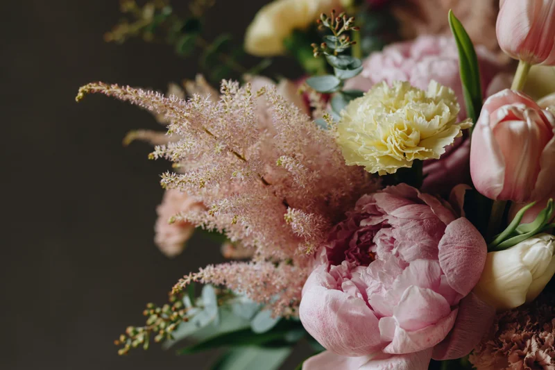 Close-up of a loose garden-style bouquet with pink peonies, tulips, astilbe and greenery arranged in soft pastel tones