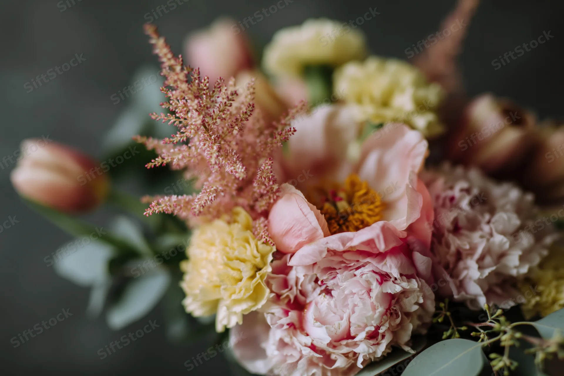 Close-up of a loose garden-style bouquet with pink peonies, yellow ranunculus, astilbe, and eucalyptus foliage