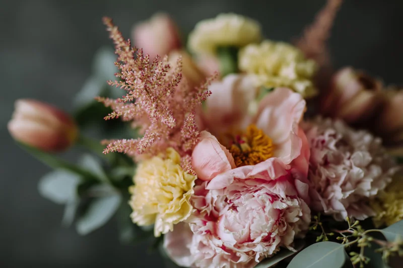 Close-up of a loose garden-style bouquet with pink peonies, yellow ranunculus, astilbe, and eucalyptus foliage