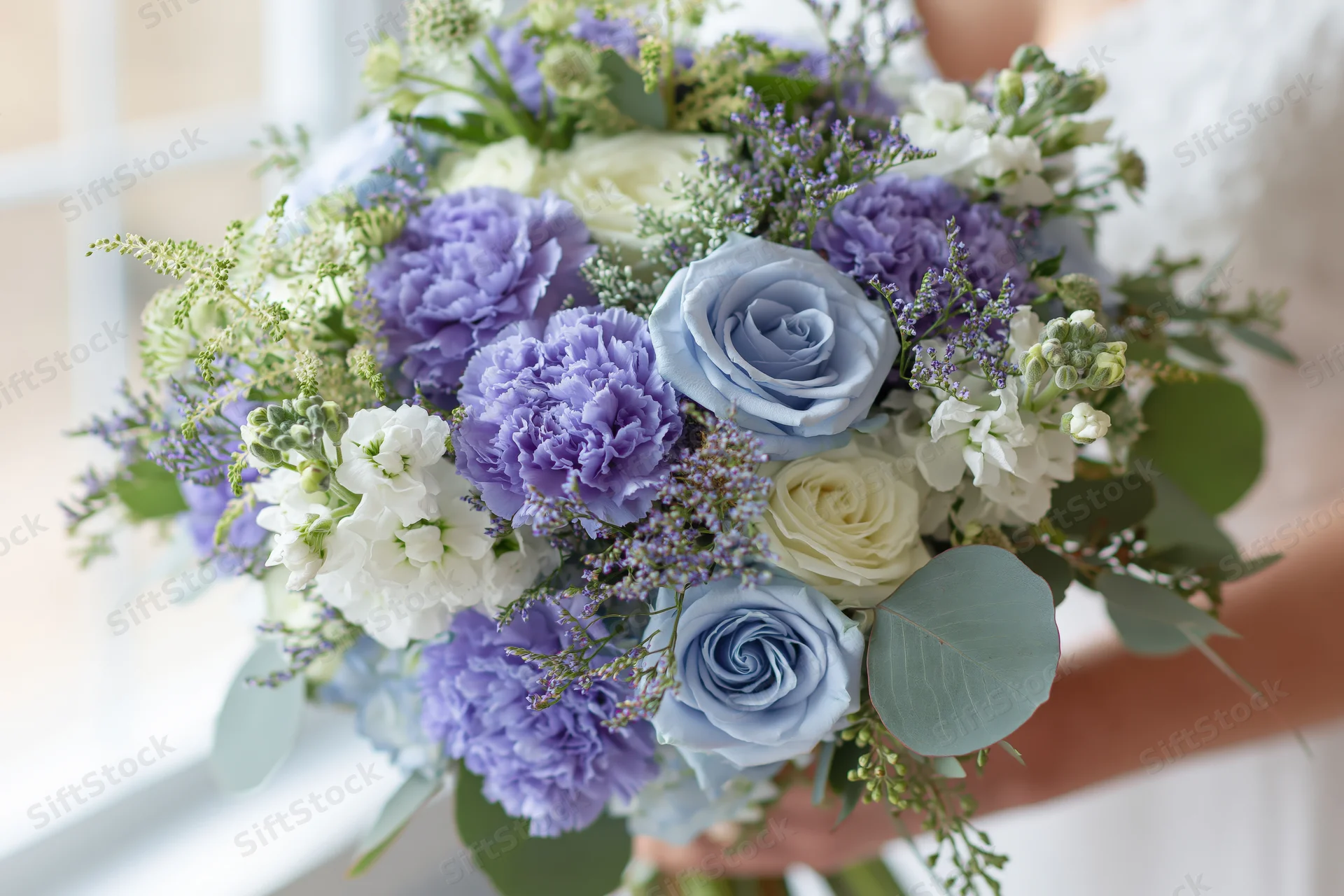 Bride holding a lush bridal bouquet of blue roses, purple hydrangeas, white flowers and greenery in soft daylight
