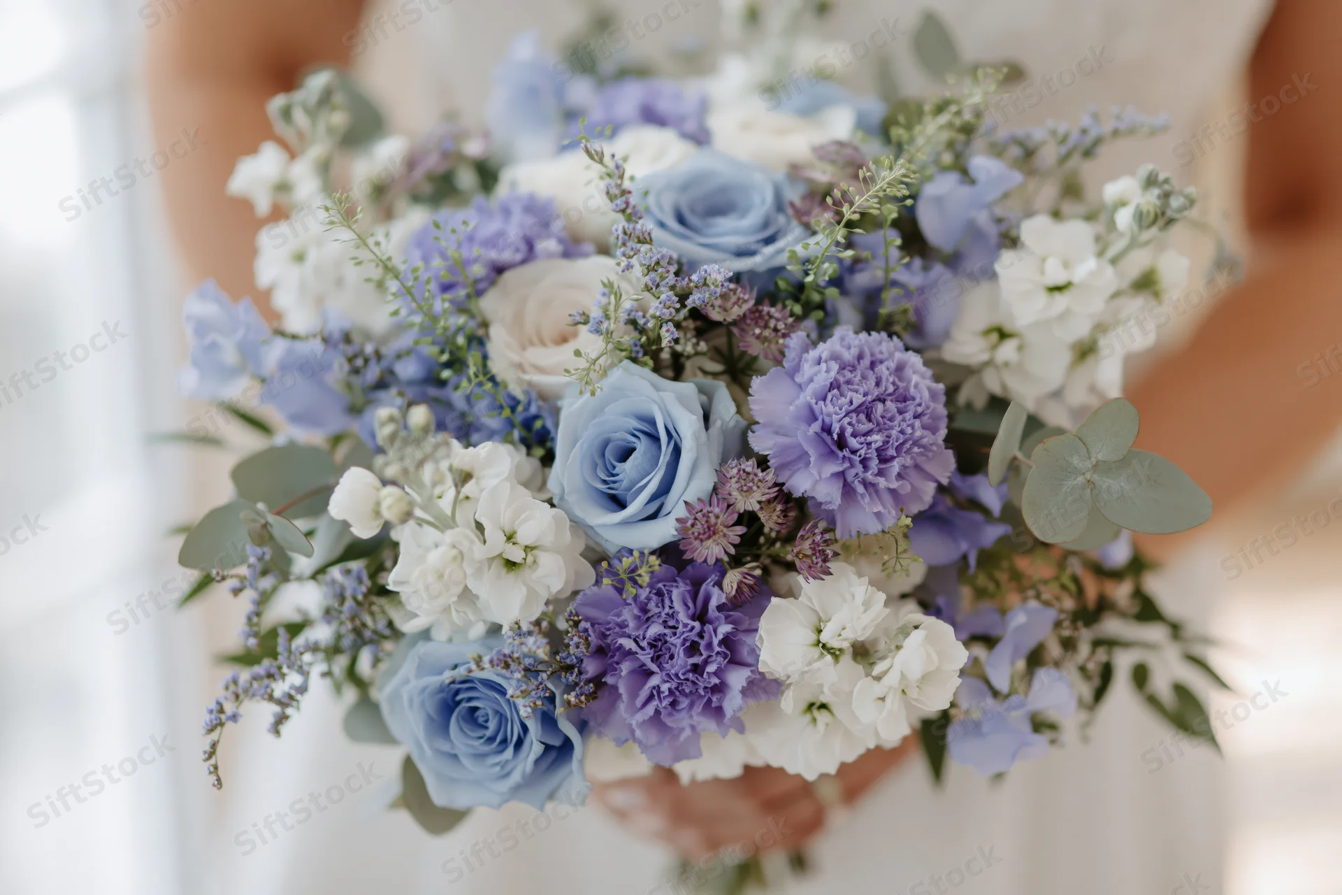 Bride holding a lush blue and white floral bouquet with roses and carnations