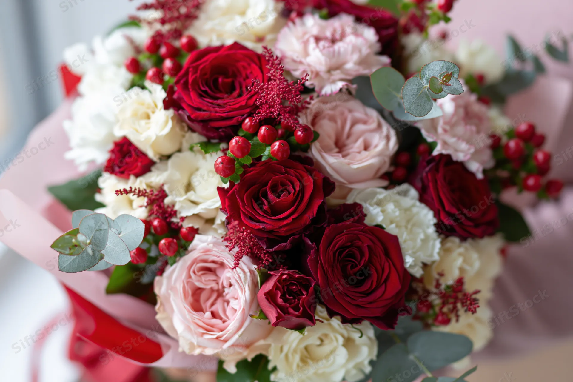 Close-up of a lush bouquet of red, pink and white roses with eucalyptus and berries wrapped in pink paper