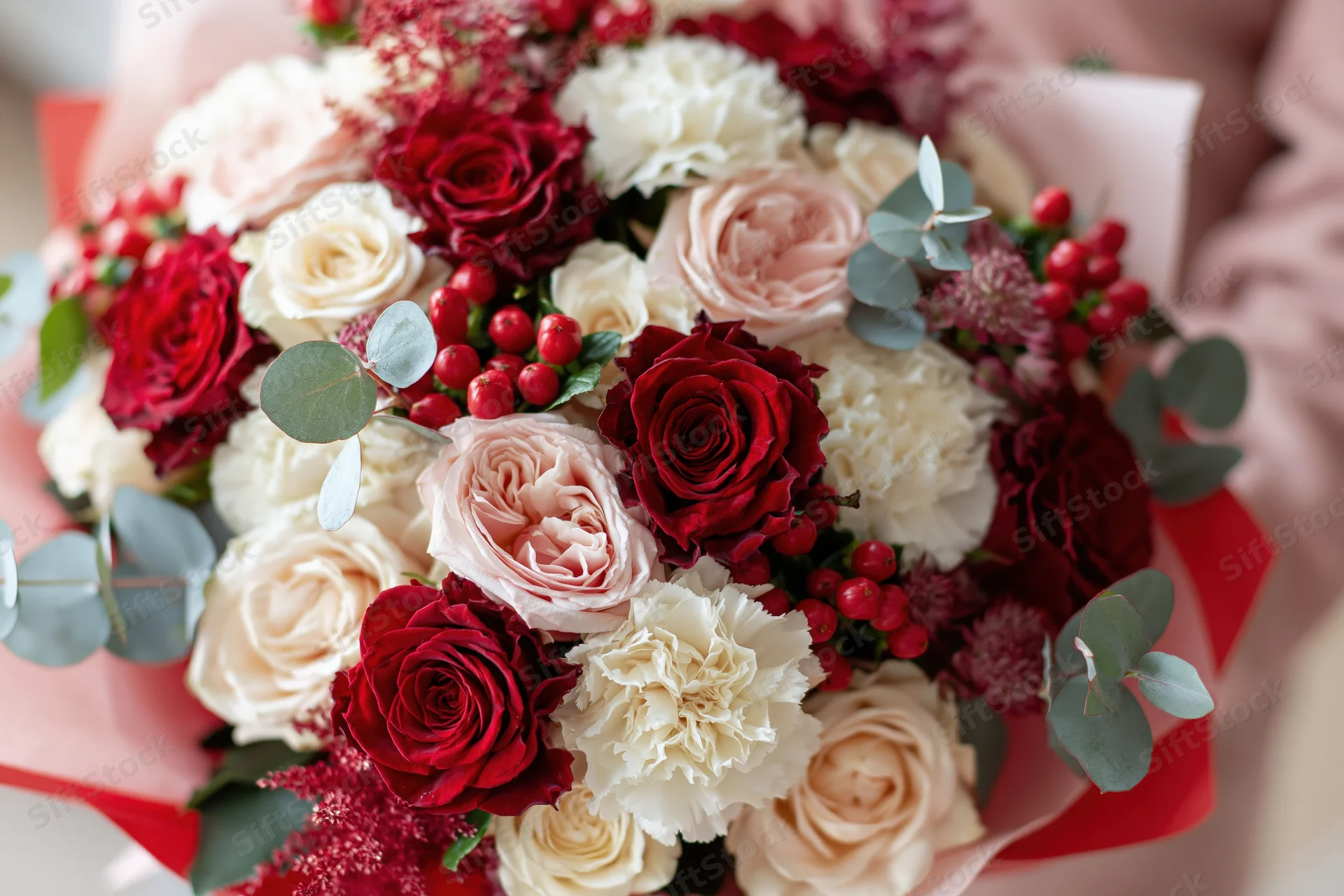 Close-up of a lush bouquet of red white and pink roses with carnations and eucalyptus held in hands