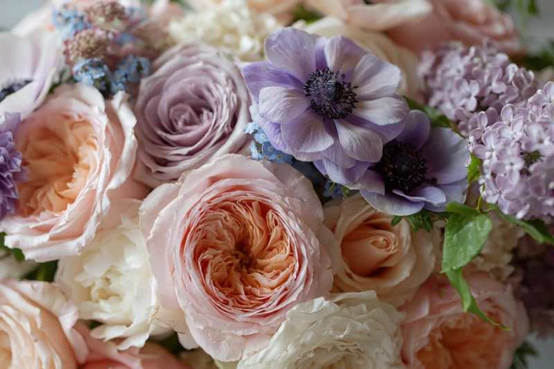 Close-up of a dense floral arrangement with pink roses, purple anemones and lilac blooms