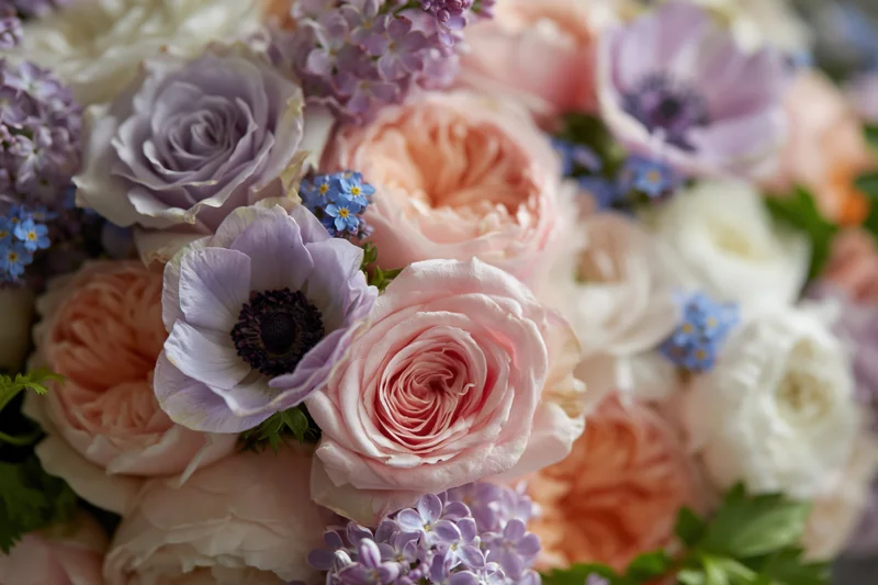 Close-up of a densely packed floral bouquet with pink roses, lavender anemones, and pastel blooms arranged with green foliage