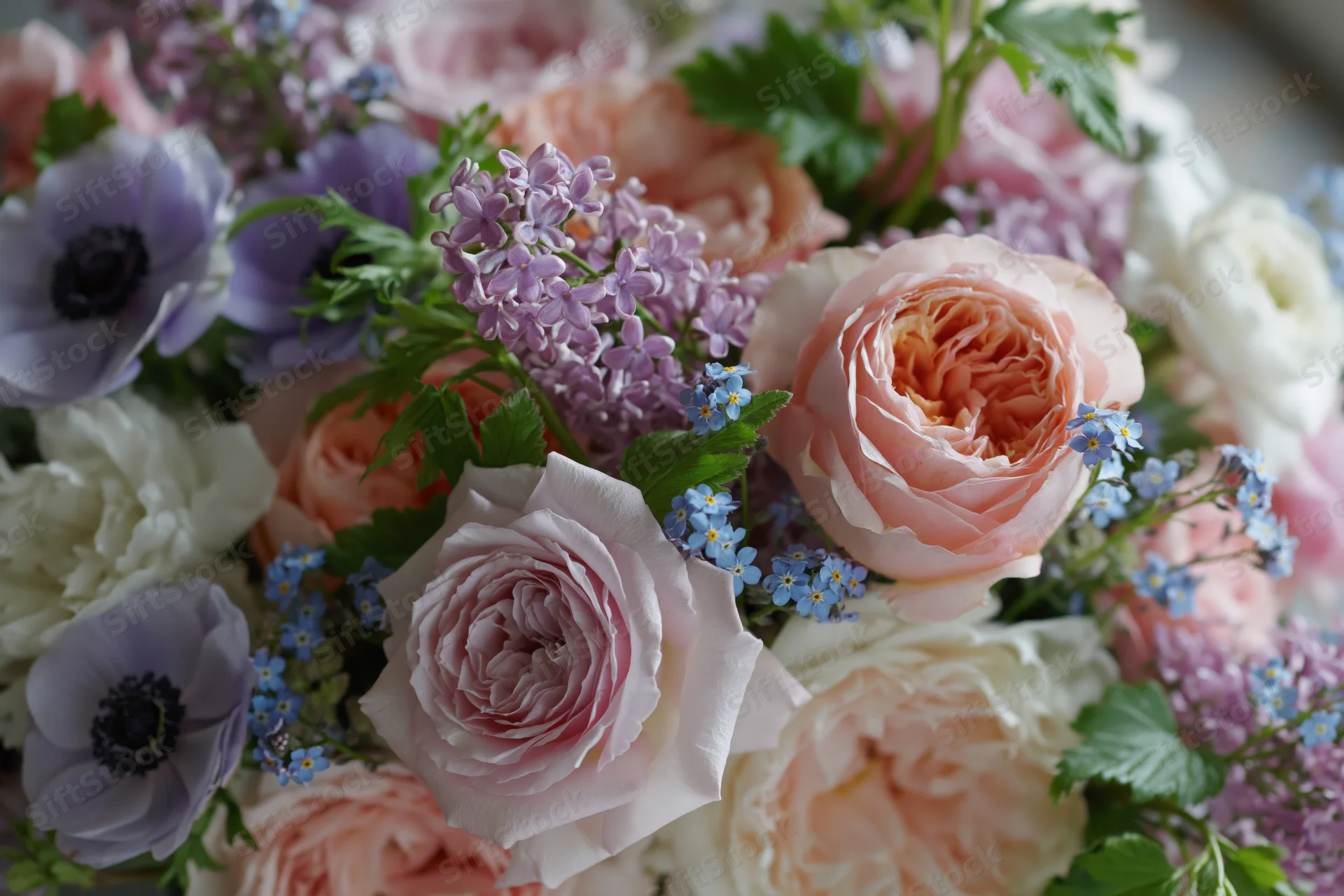 Close-up of a dense floral bouquet with roses, peonies, anemones, lilac and forget-me-nots in soft pastel colors
