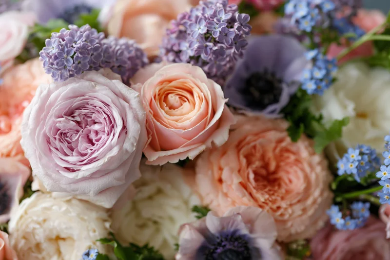 Close-up of a dense mixed floral arrangement with roses, peonies, anemones, lilac and forget-me-nots in soft pastel colors