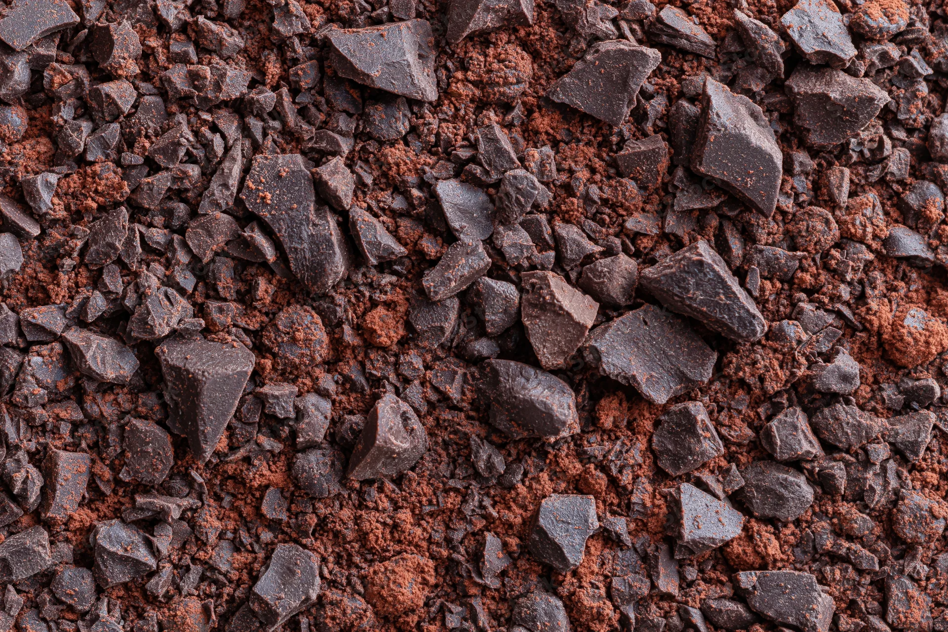 Crushed dark chocolate pieces and fine cocoa powder scattered across a flat surface in a close-up top-down view