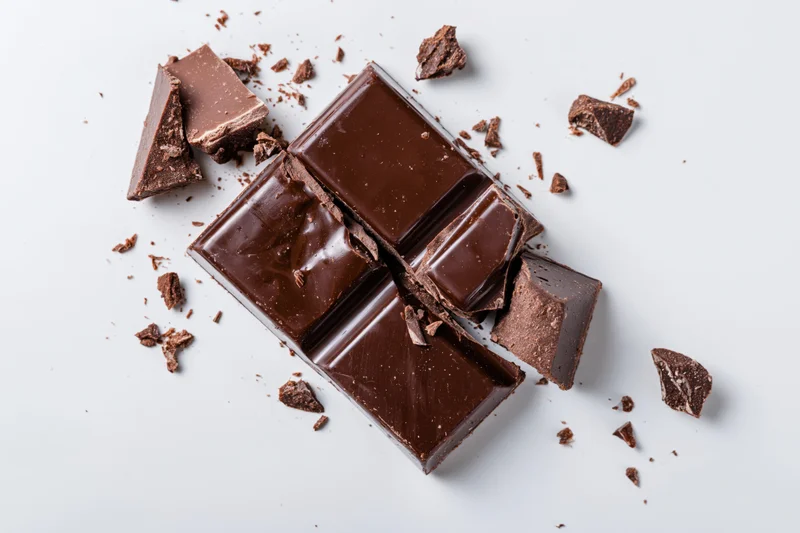 Broken dark chocolate bar with scattered pieces and crumbs on white background