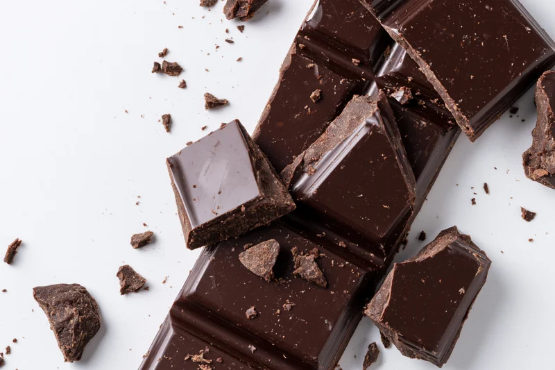 Broken dark chocolate bar with crumbs on white background