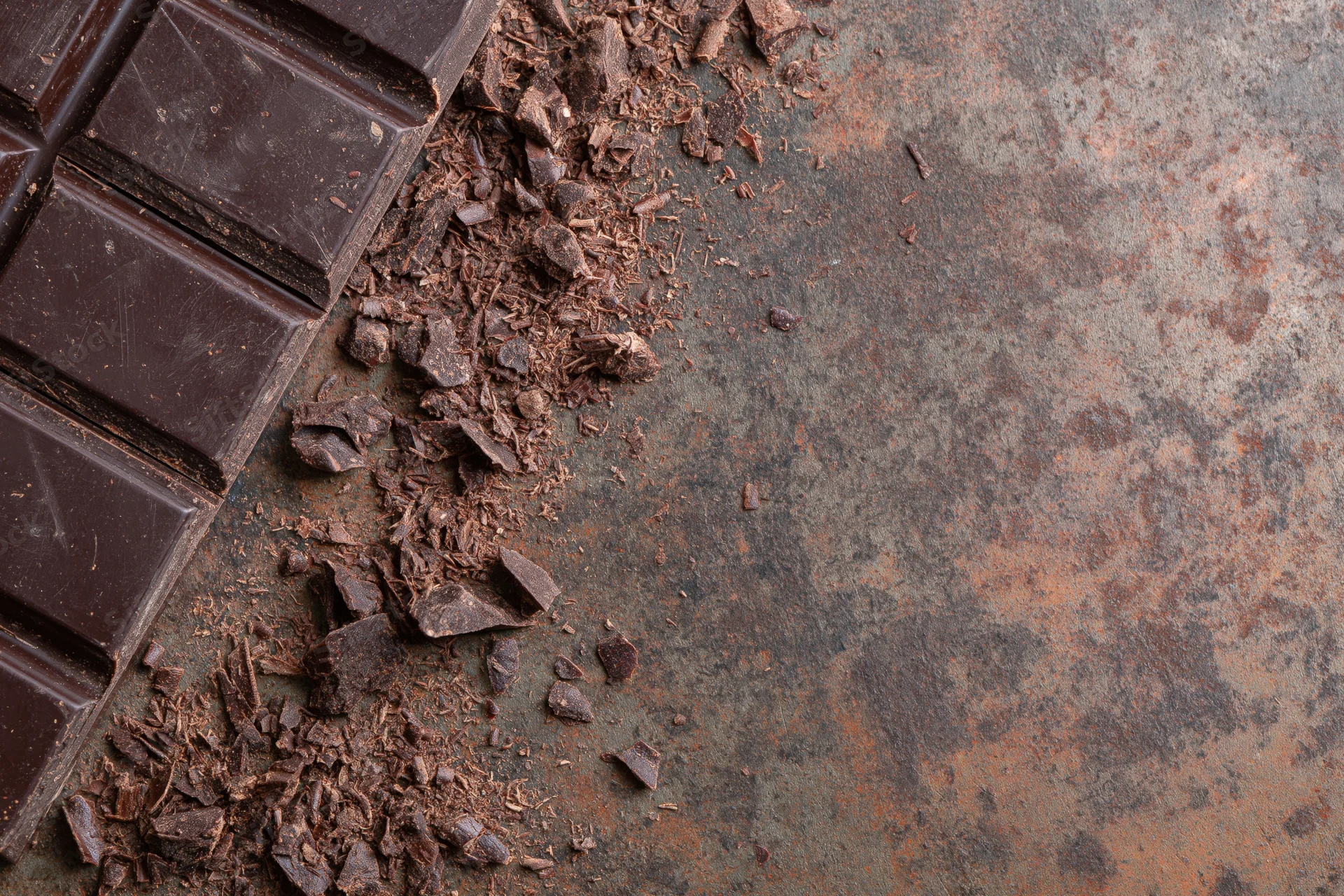 Dark chocolate bar broken into squares and crumbs on a rusted metal surface