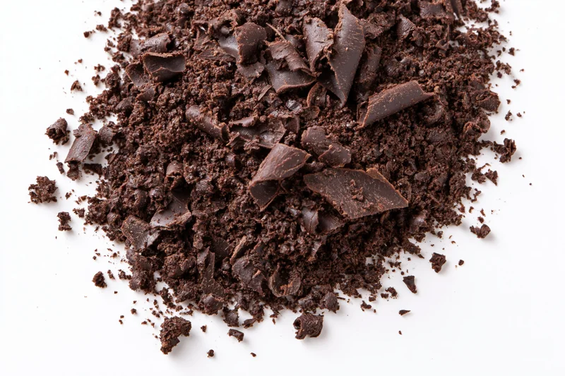 Dark chocolate shavings and crumbled pieces scattered in a pile on white background