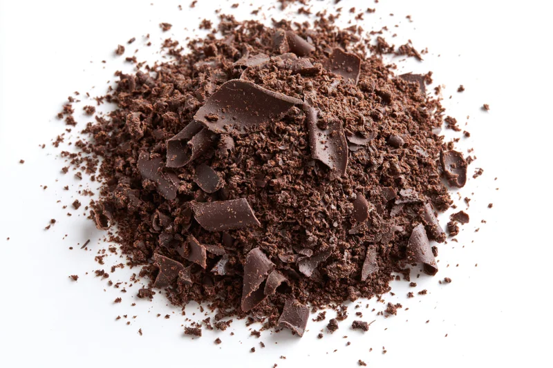 Pile of dark chocolate shavings and crumbled pieces scattered on white background