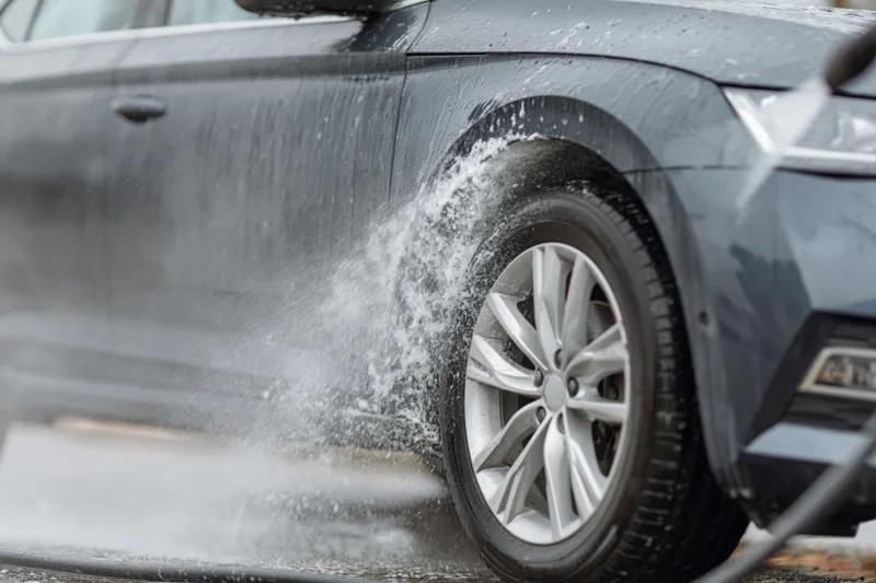 Dark grey sedan being sprayed with pressure washer wand near front wheel