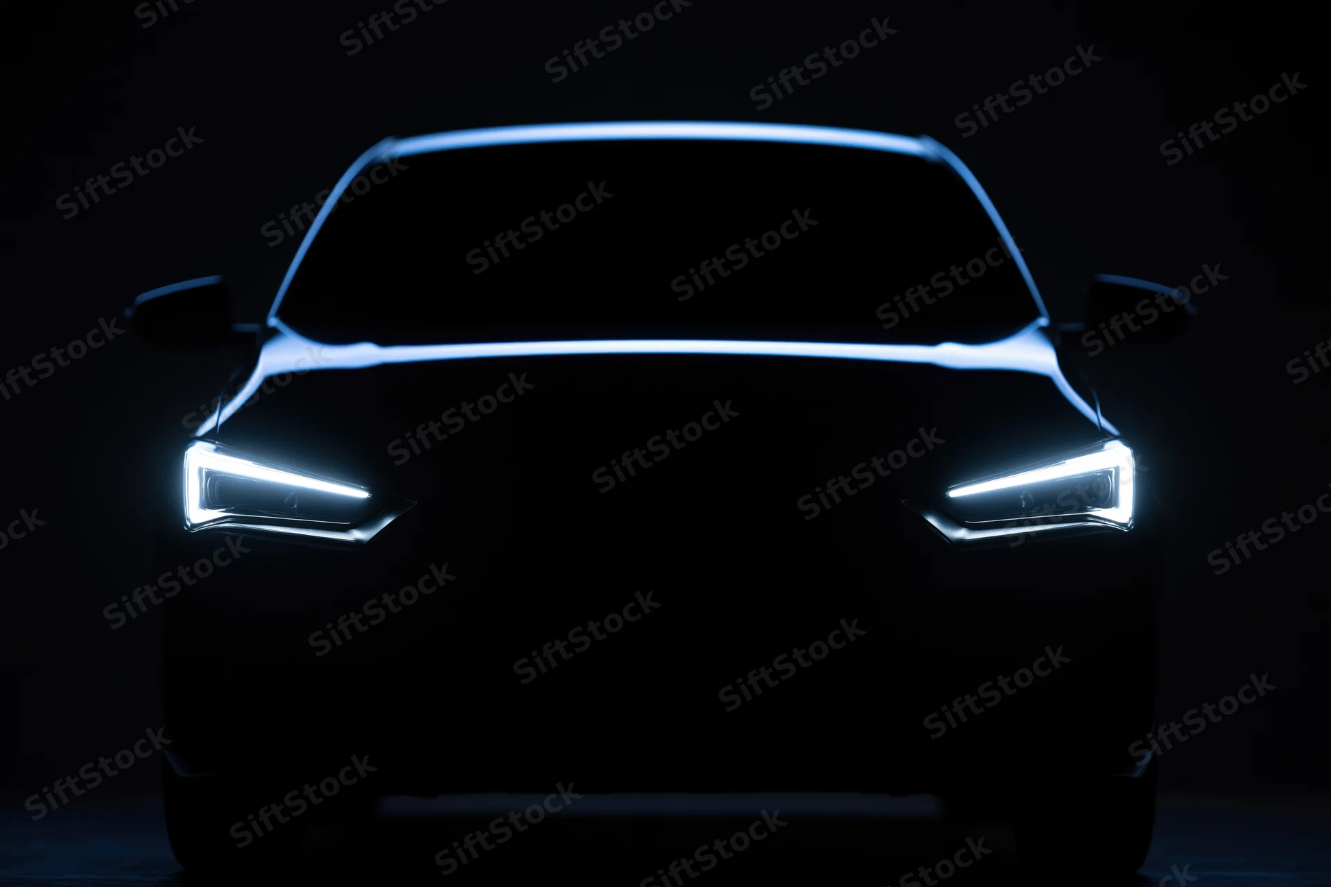 Modern sedan silhouette facing forward with glowing led headlights in dark studio