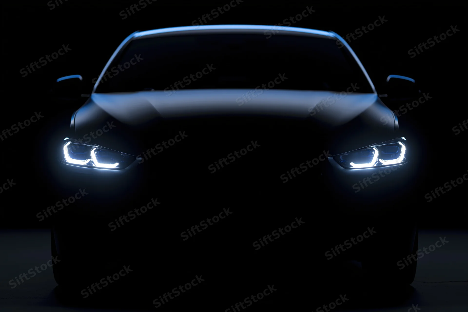 Modern sedan facing forward with illuminated led headlights in dark studio setting