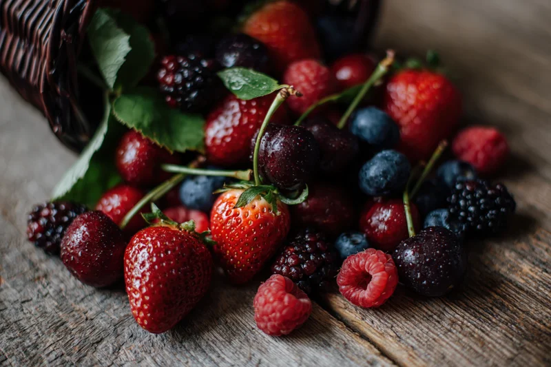 Strawberries and mixed berries spilling from a dark wicker basket onto a rustic wooden table