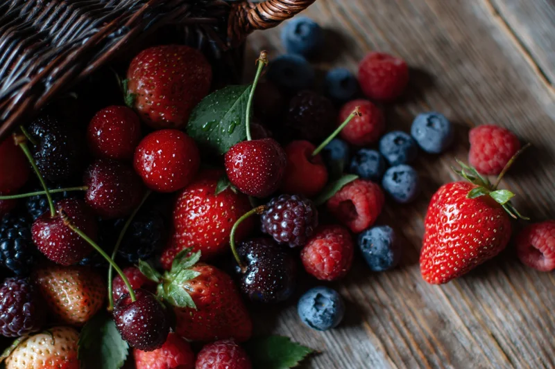 Dark wicker basket tipped over spilling mixed berries onto wooden surface