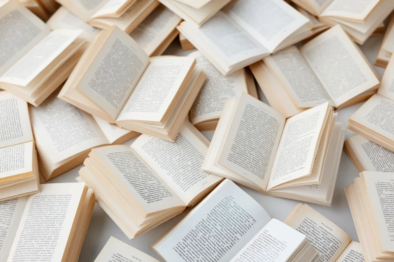 Open hardcover books scattered across a white surface in disarray