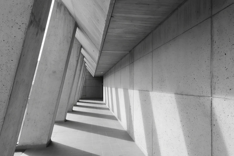 Long concrete corridor with angled columns and strong shadows creating geometric perspective
