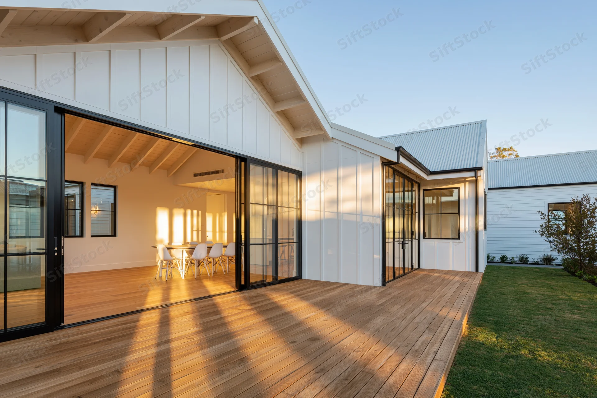 Modern farmhouse home exterior with sliding glass doors opening to wooden deck and dining area visible inside