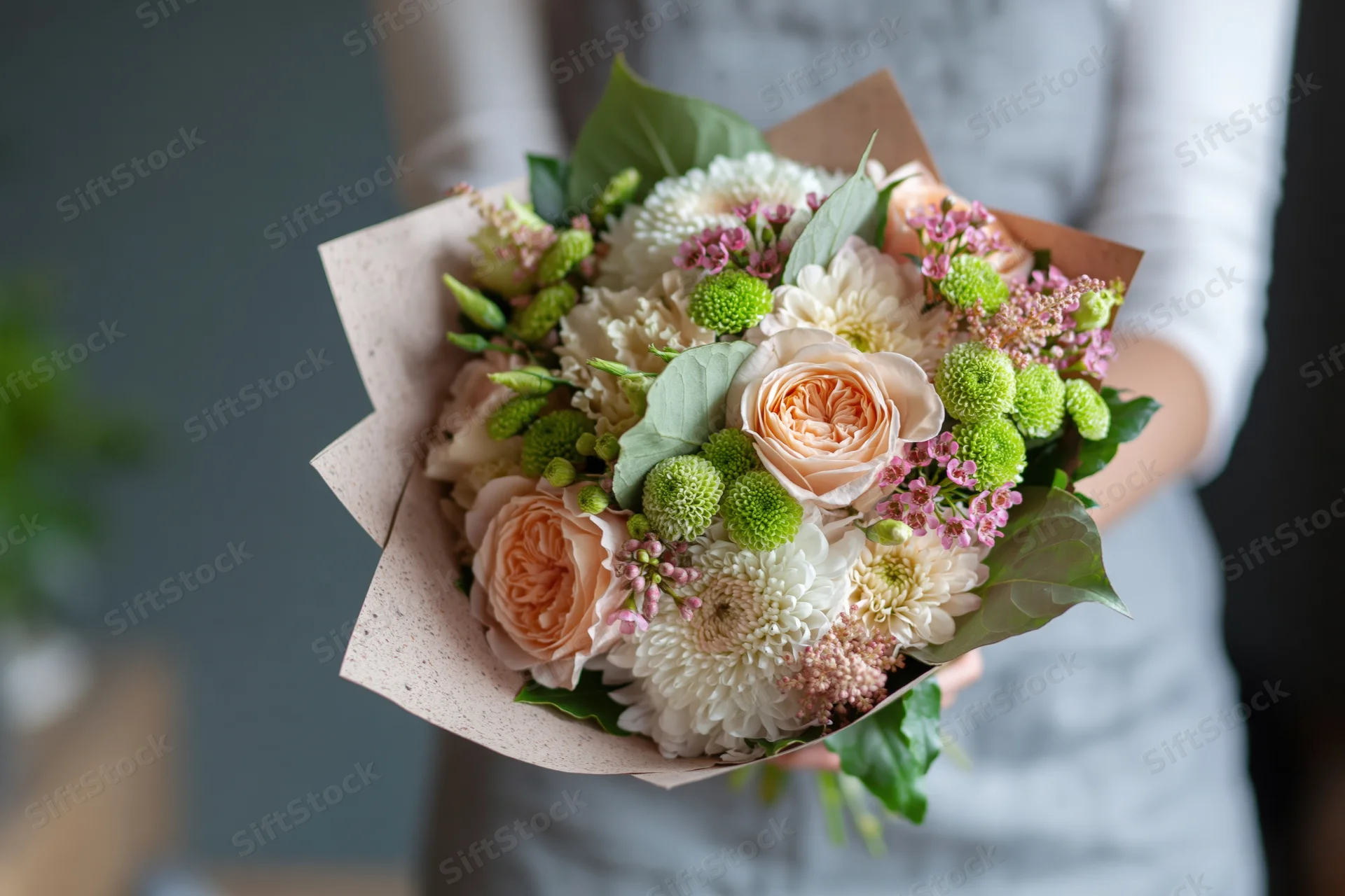Woman holding a mixed flower bouquet wrapped in paper at chest height