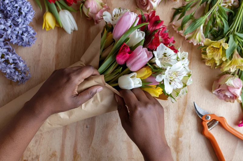Florist hands wrapping a mixed bouquet in kraft paper on a wooden table