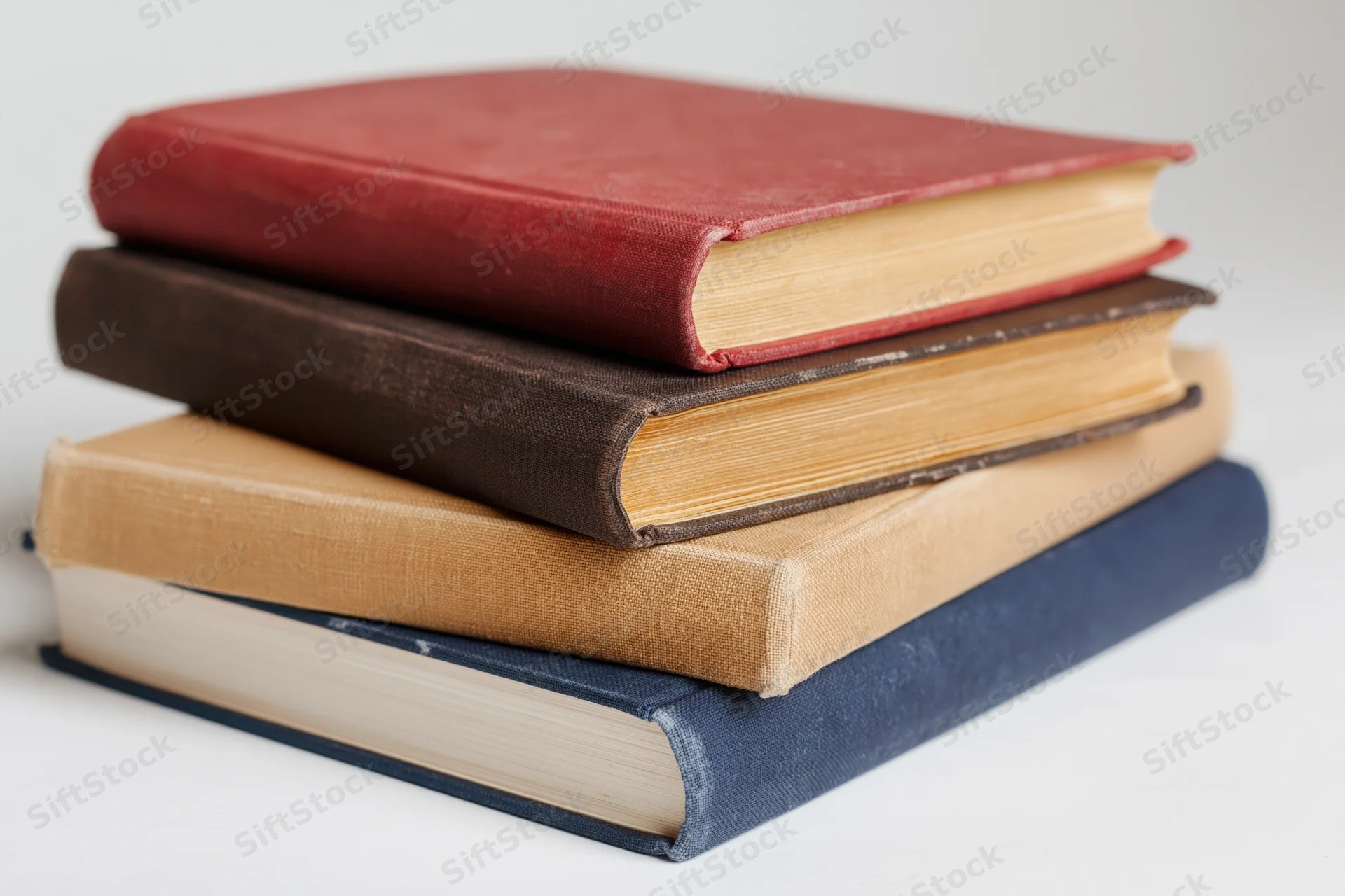 Four hardcover books stacked unevenly on a plain white surface