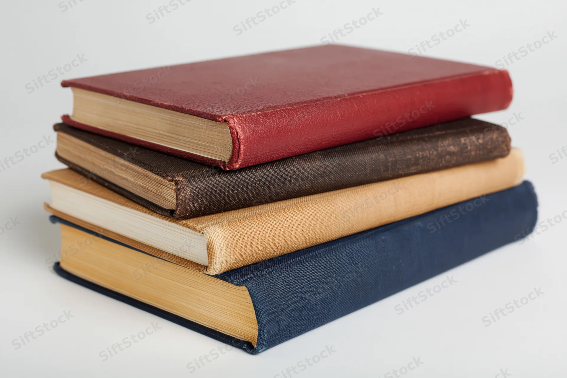 Stack of four hardcover books in red, brown, beige and blue arranged unevenly on white surface