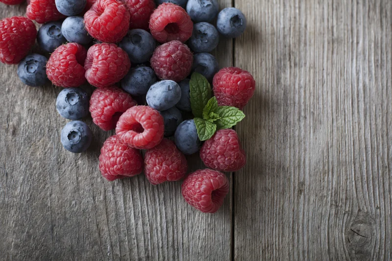 Raspberries and blueberries with mint leaves scattered on a rustic wooden surface