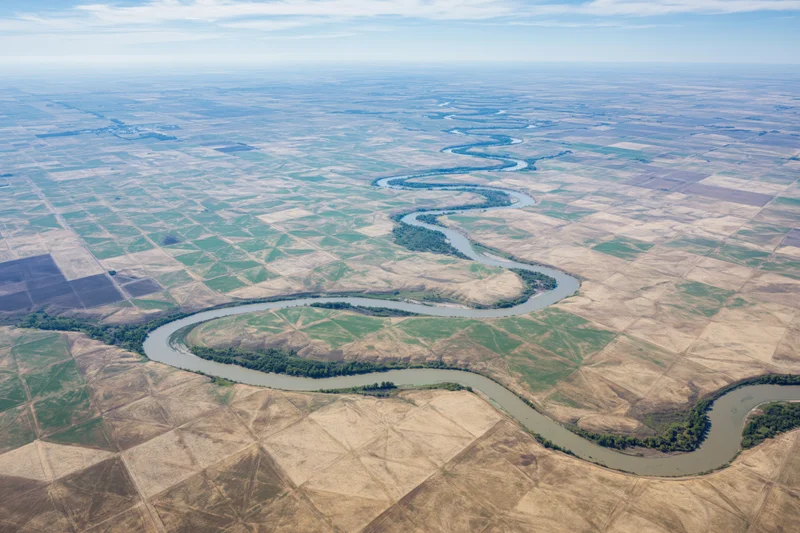 Meandering river winding through farmland fields from aerial view