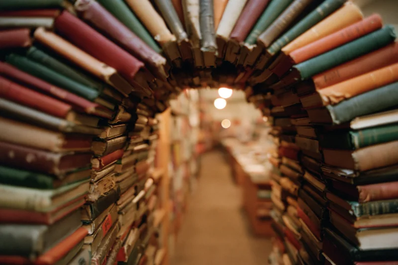 Stacks of vintage books forming an archway tunnel in a cozy bookstore interior