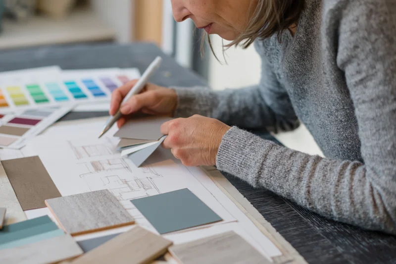 Interior designer sketching a room layout on paper with color and material samples on a dark desk