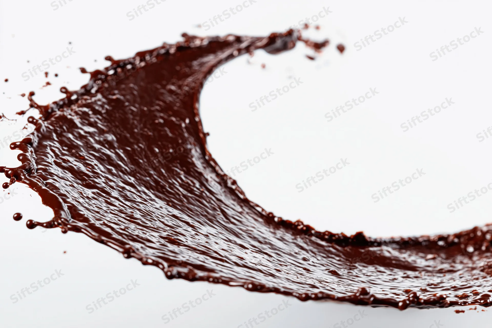 Dark chocolate liquid splashing in dynamic arc frozen in motion against white background