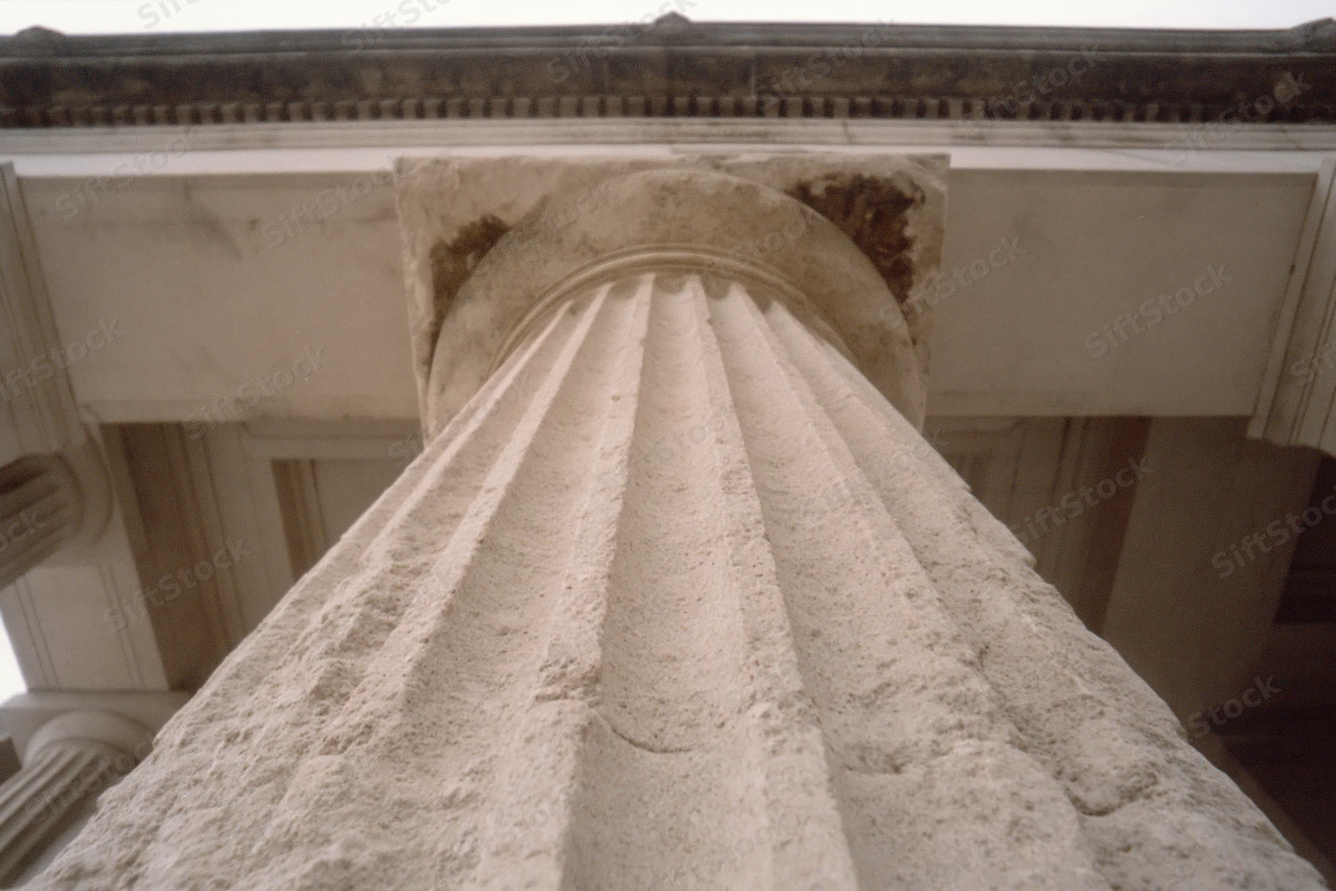 Low-angle view of a fluted stone column base and shaft under an entablature in neoclassical architecture