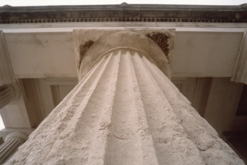 Low-angle view of a fluted stone column base and shaft under an entablature in neoclassical architecture