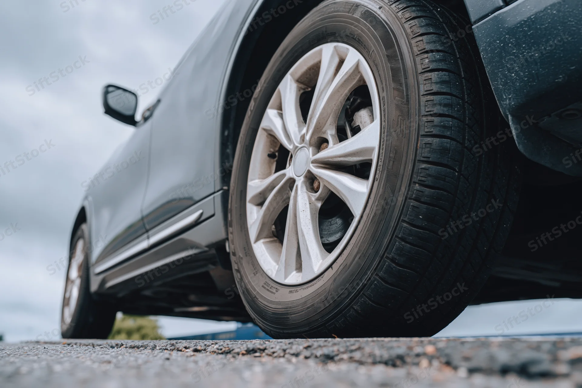 Low-angle close-up of a dark gray suv's front wheel and alloy rim on asphalt road