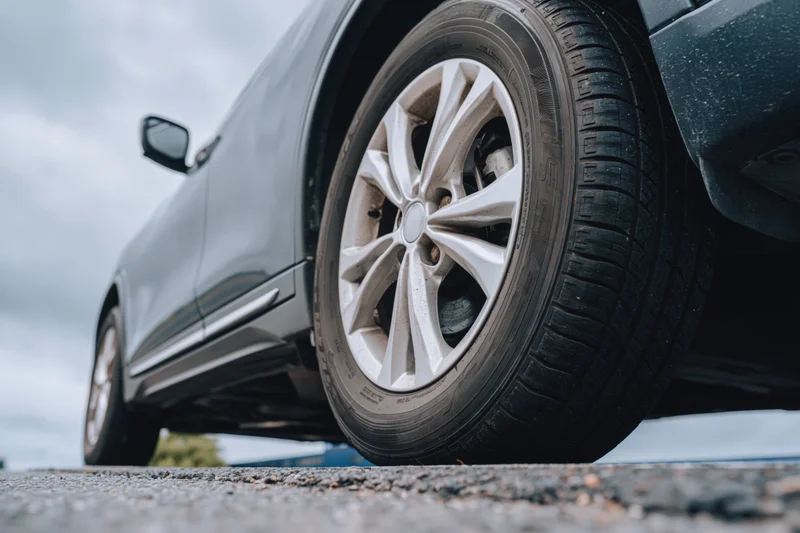 Low-angle close-up of a dark gray suv's front wheel and alloy rim on asphalt road